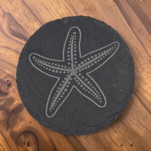 Round 4-inch charcoal slate coaster featuring a laser-engraved five-arm starfish with dotted details, displayed on a wooden table.