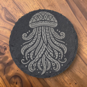 Round 4-inch dark slate coaster with intricate laser-engraved jellyfish design, displayed on a natural wooden surface.