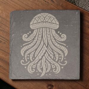 Square 4-inch slate coaster featuring intricate laser-engraved jellyfish artwork on dark gray stone, displayed on a wooden table.