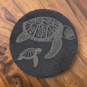 Round Hawaiian honu slate coaster with detailed laser-engraved mother and baby sea turtles on dark stone.