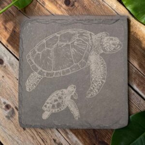 Square slate coaster with laser-engraved mother and baby sea turtles swimming together on dark gray stone.